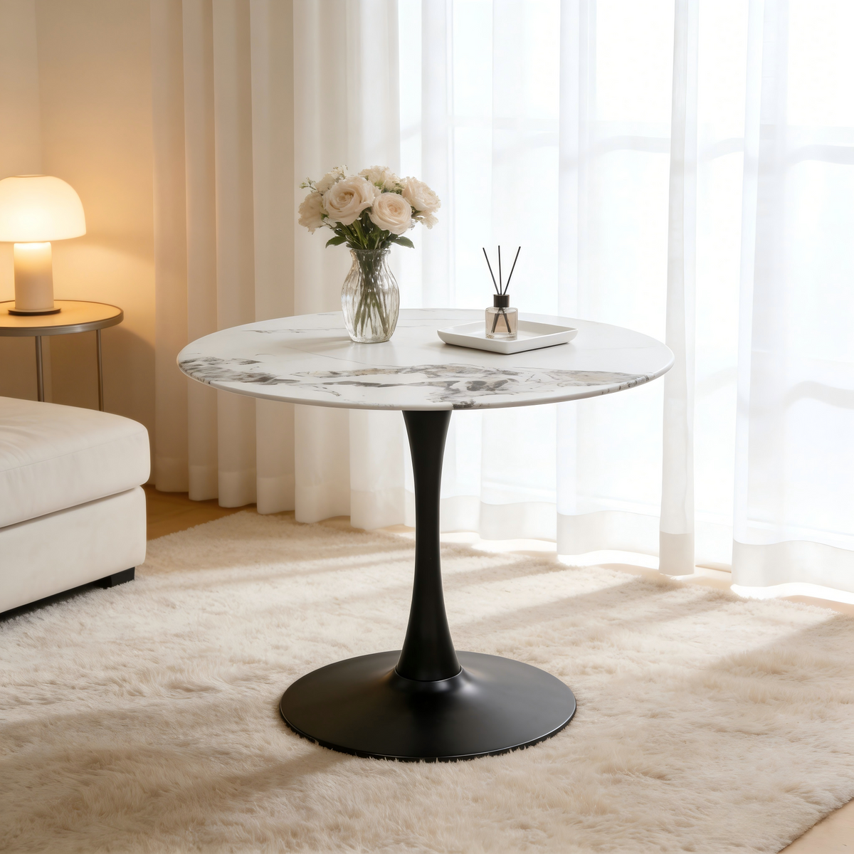Faux marble tulip dining table with black pedestal styled with roses beside a lamp