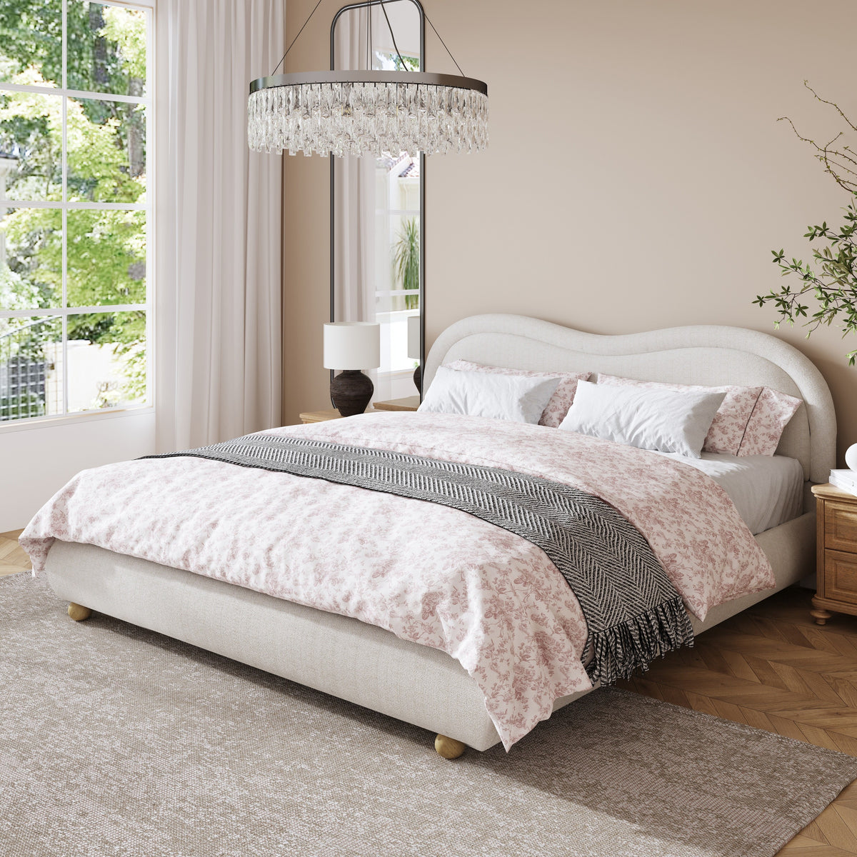 Angled beige chenille platform bed with pink floral bedding under a crystal chandelier