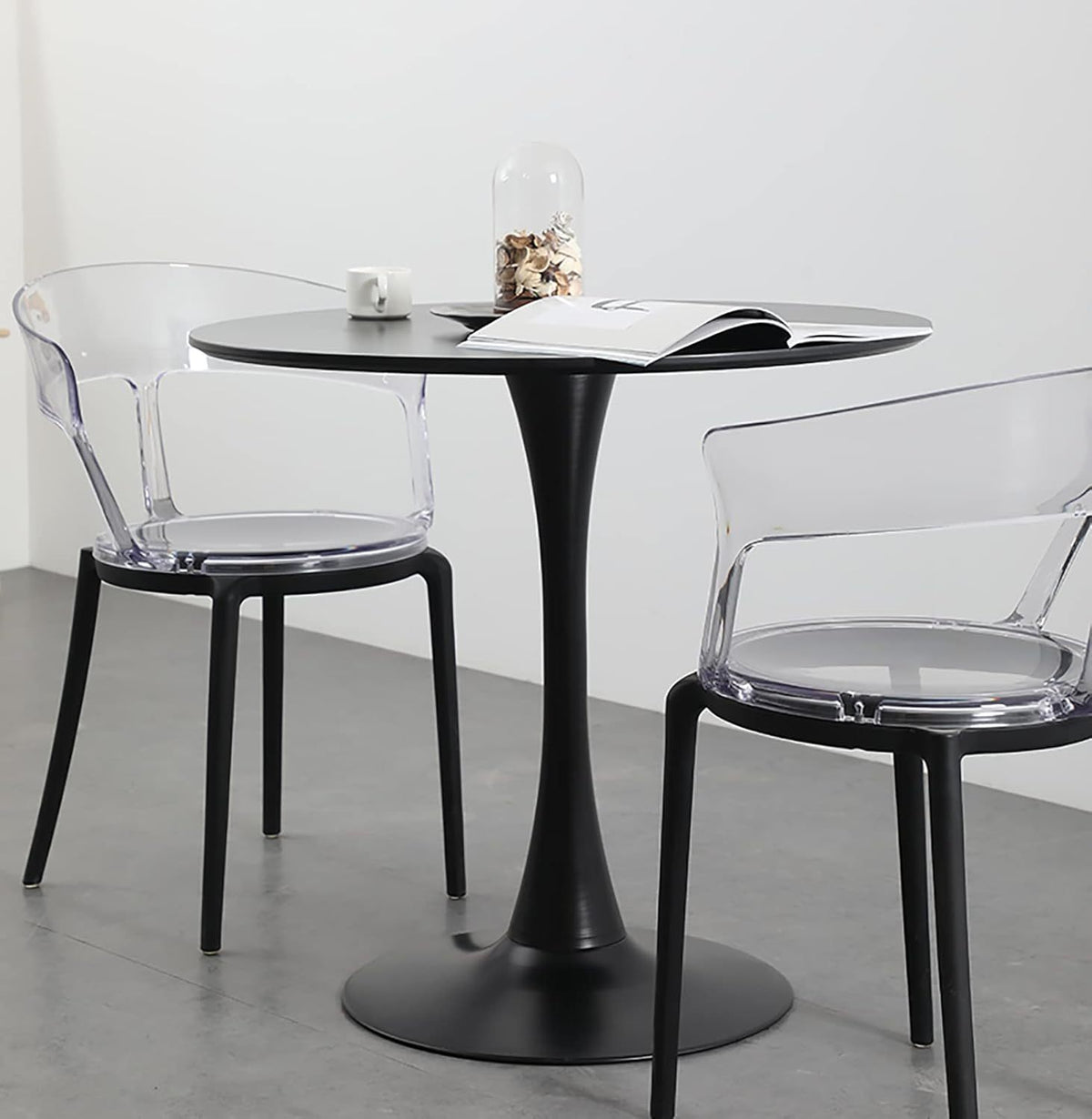 Round black tulip table with two clear armchairs, a mug and an open book