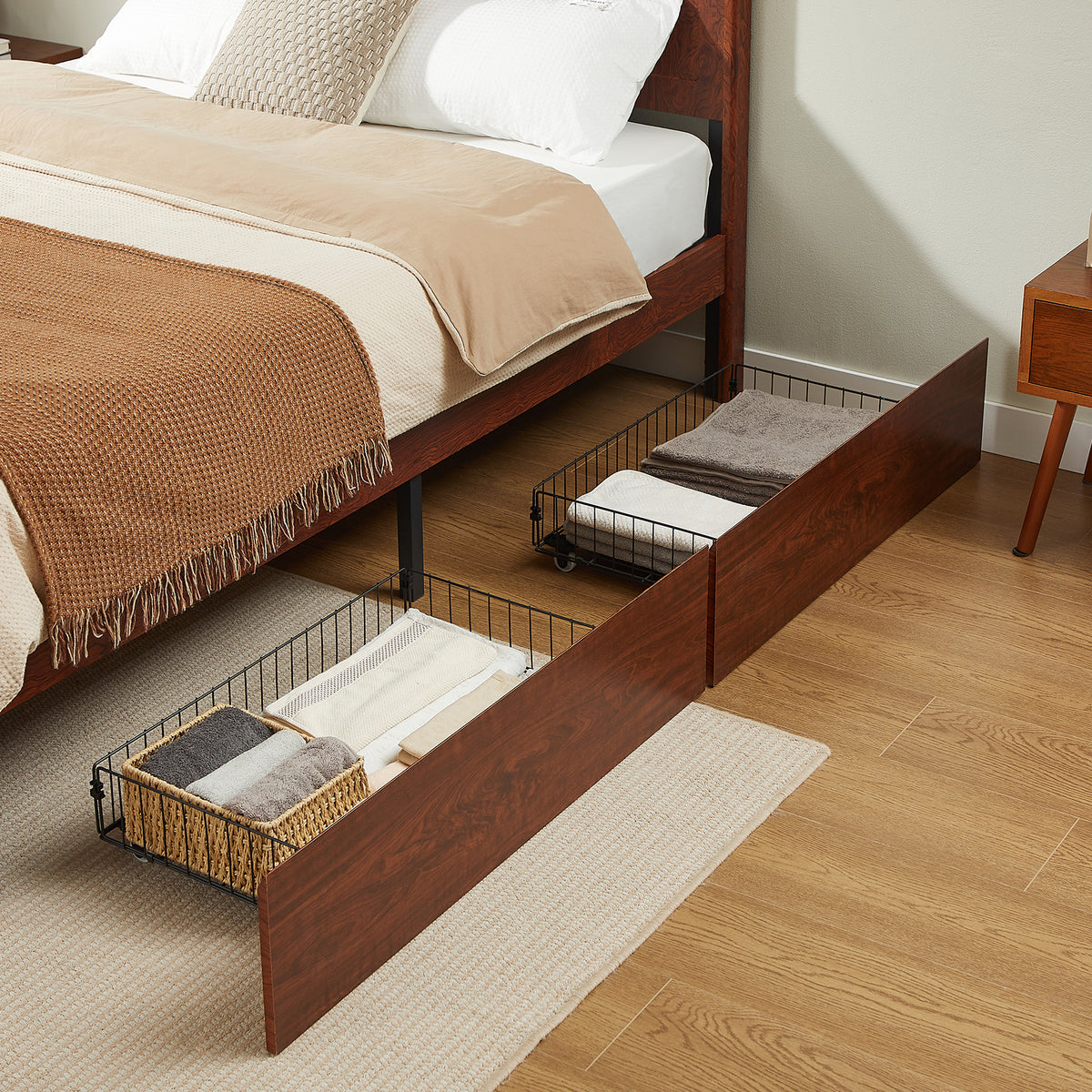 Two side storage drawers pulled out under dark reddish-brown wood bed, holding folded towels and baskets