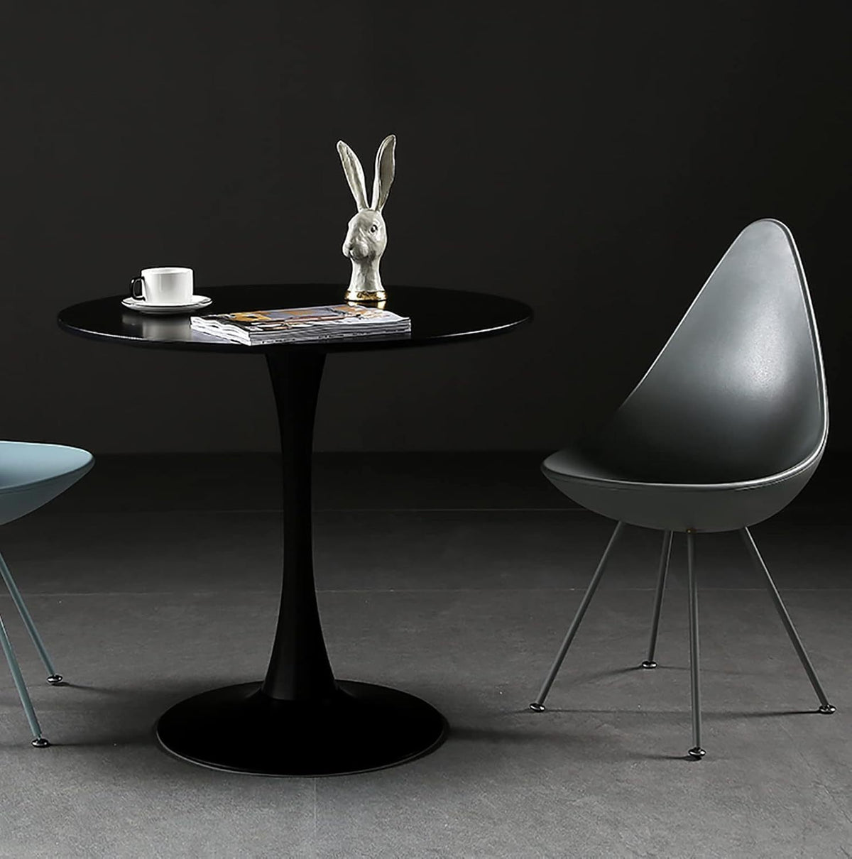 Black round dining table in a dark studio styled with a coffee cup and rabbit bust beside a gray chair