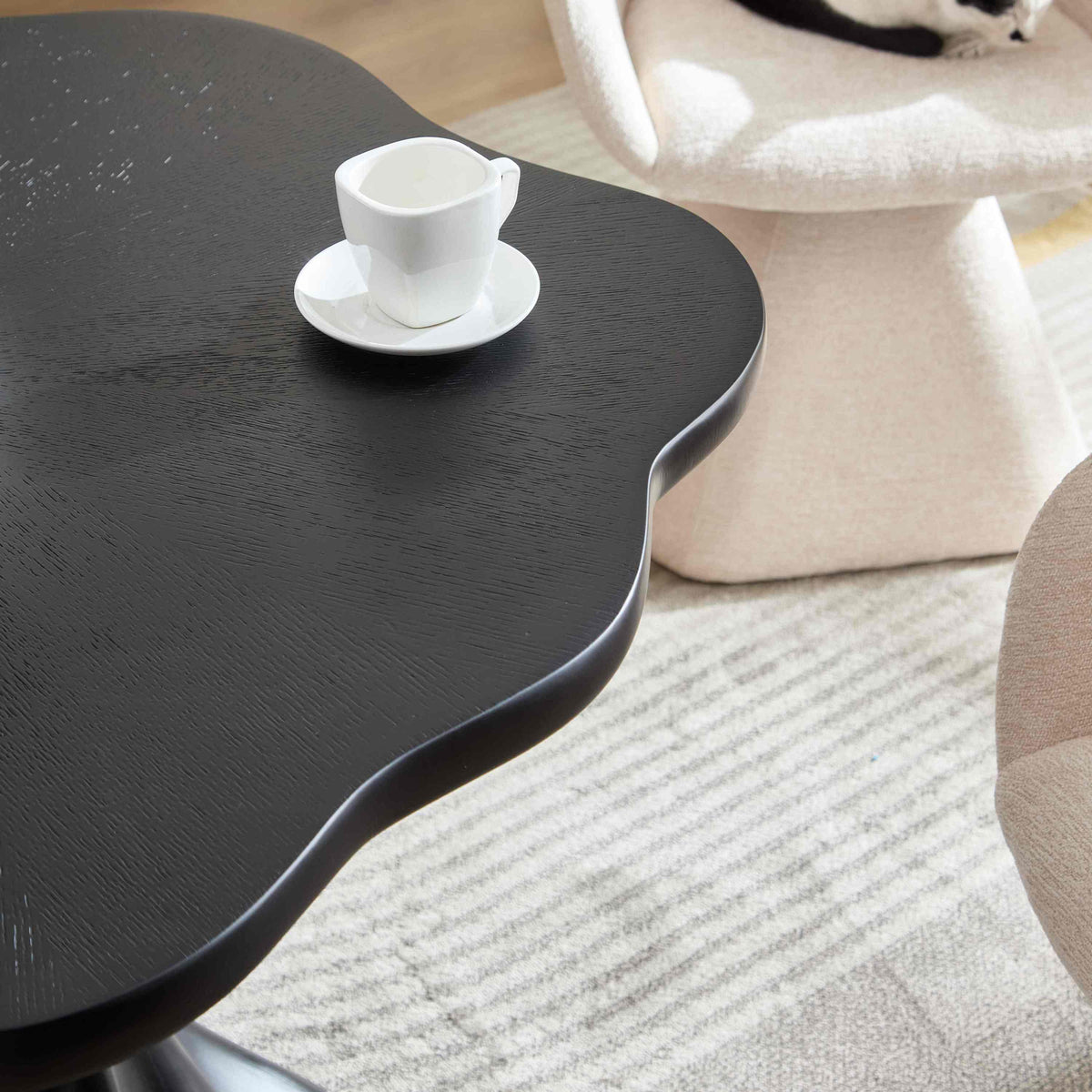 Overhead close-up of the black petal tabletop corner with an espresso cup, boucle chairs around