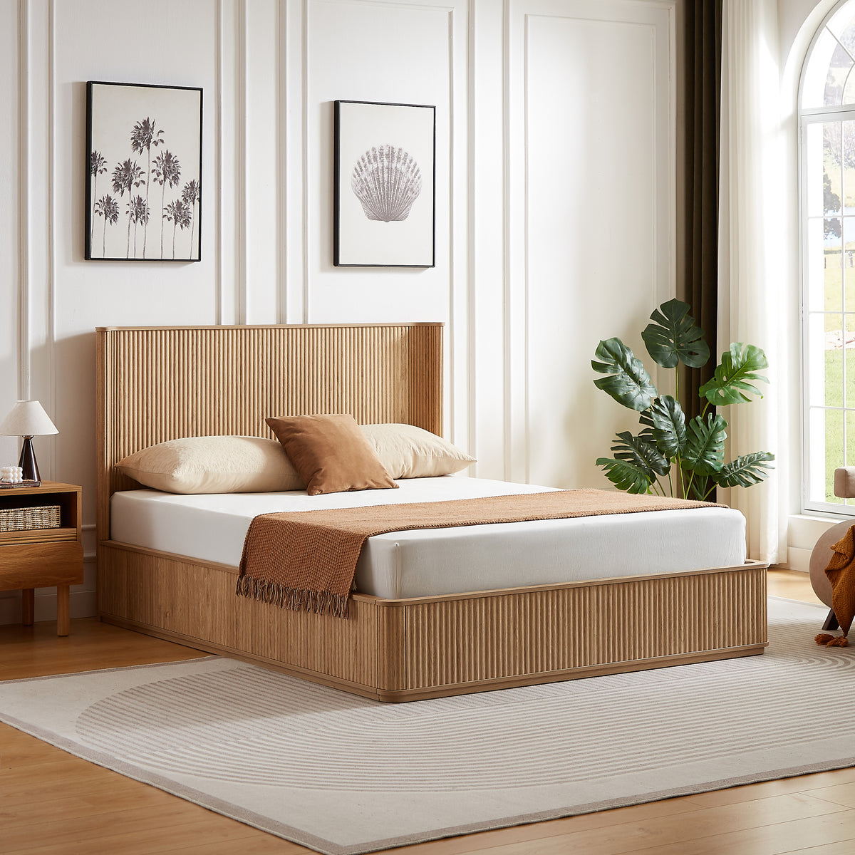 Angled view of the natural oak fluted queen platform bed by an arched window with a monstera plant
