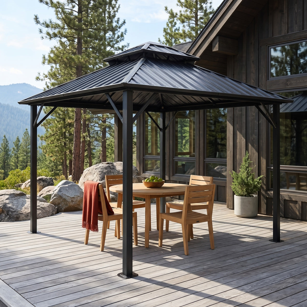 Gray 10x10 hardtop gazebo with double tier roof over a teak dining set on a wood deck by a mountain house