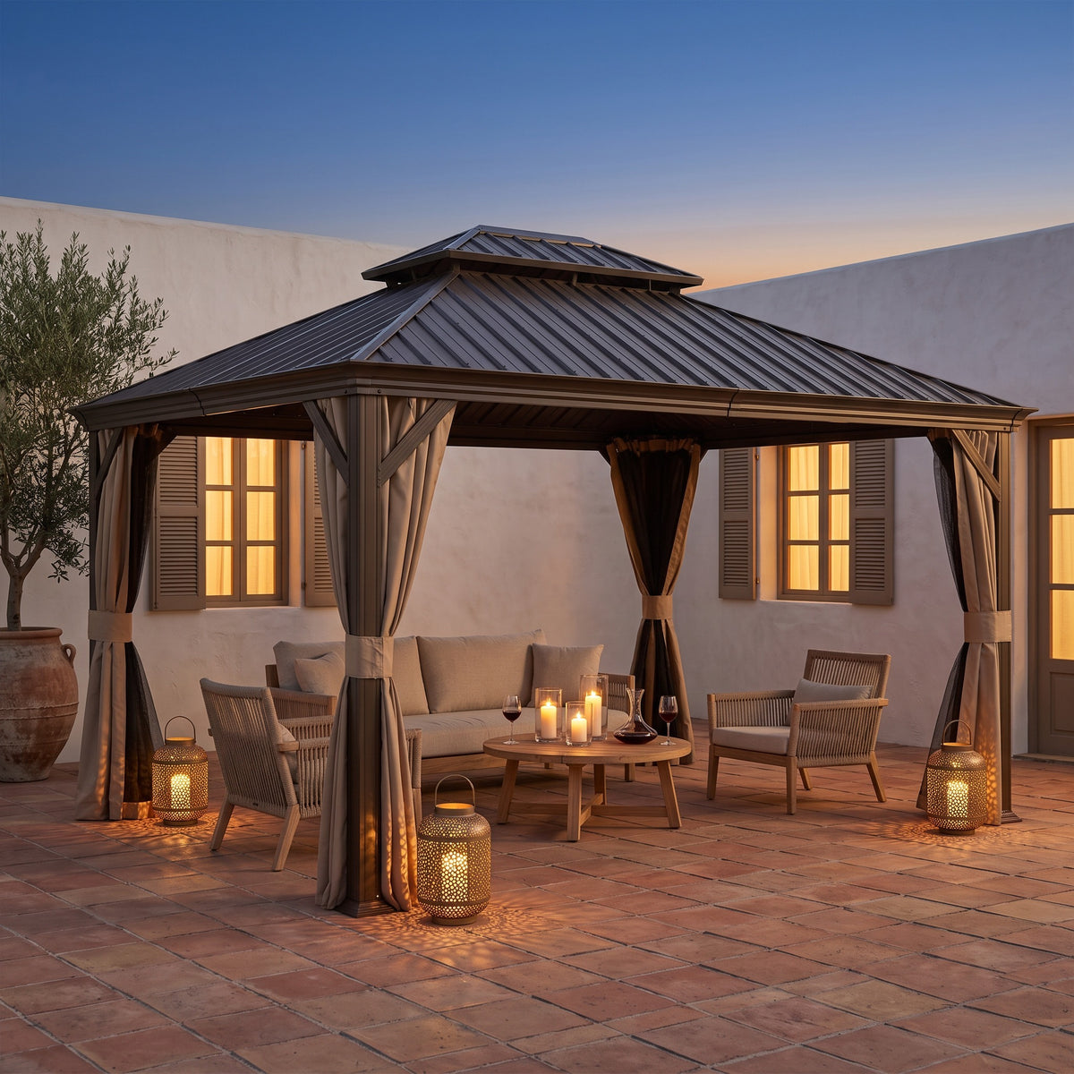 Brown metal 10x13 double roof hardtop gazebo with tied back curtains over a sofa and lanterns in a tile courtyard at dusk