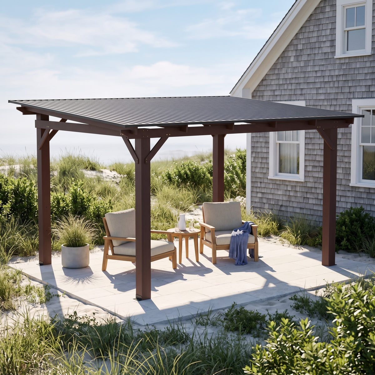 Brown wood patio gazebo with a dark gray metal roof over two lounge chairs on a stone patio by a shingled house