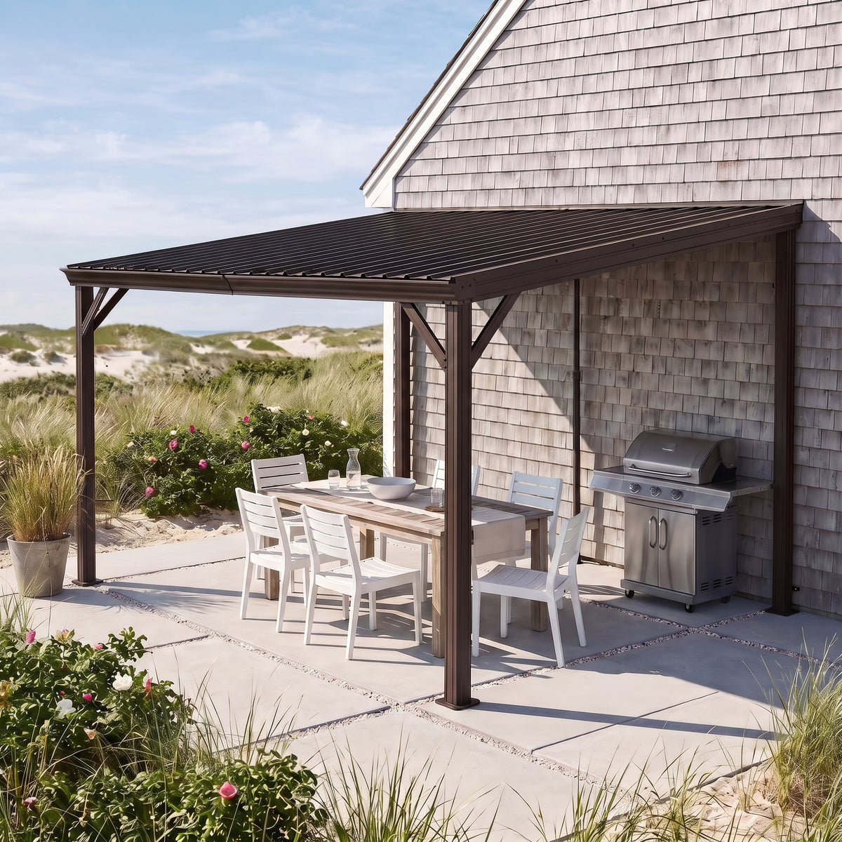 Brown metal lean-to hardtop gazebo against a shingled house over a white dining set and grill on a sunny beach patio