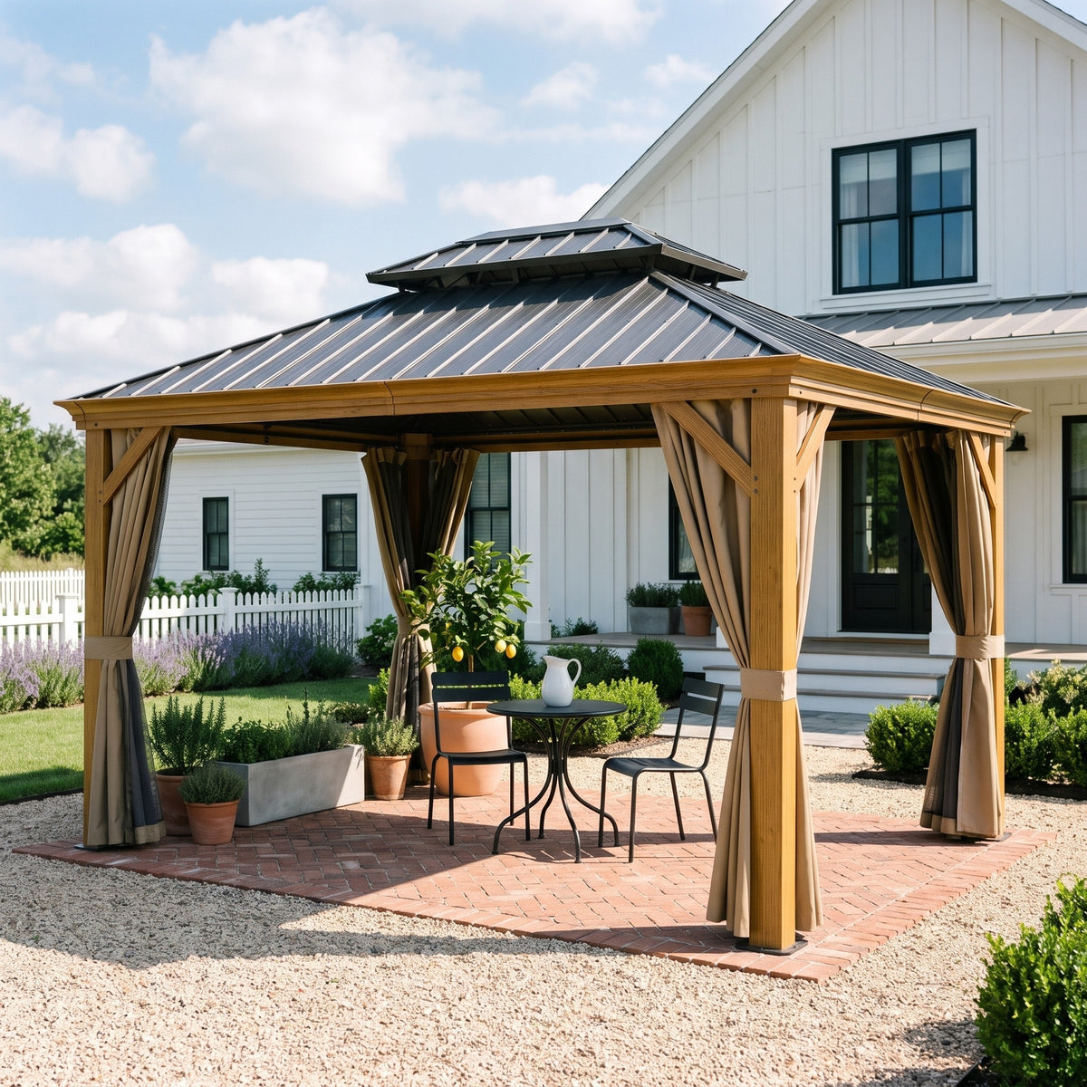 Wood grain aluminum 10x14 hardtop gazebo with tan curtains over a bistro set on a brick patio beside a white farmhouse