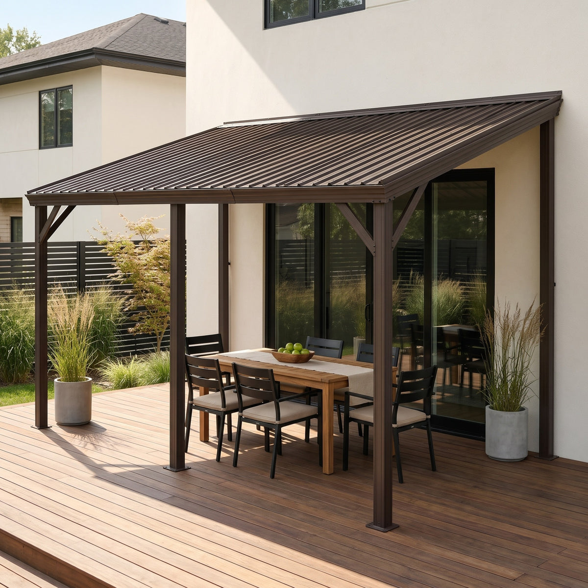 Brown steel 10x16 lean-to hardtop gazebo against a white house, over a teak dining table on a wood deck