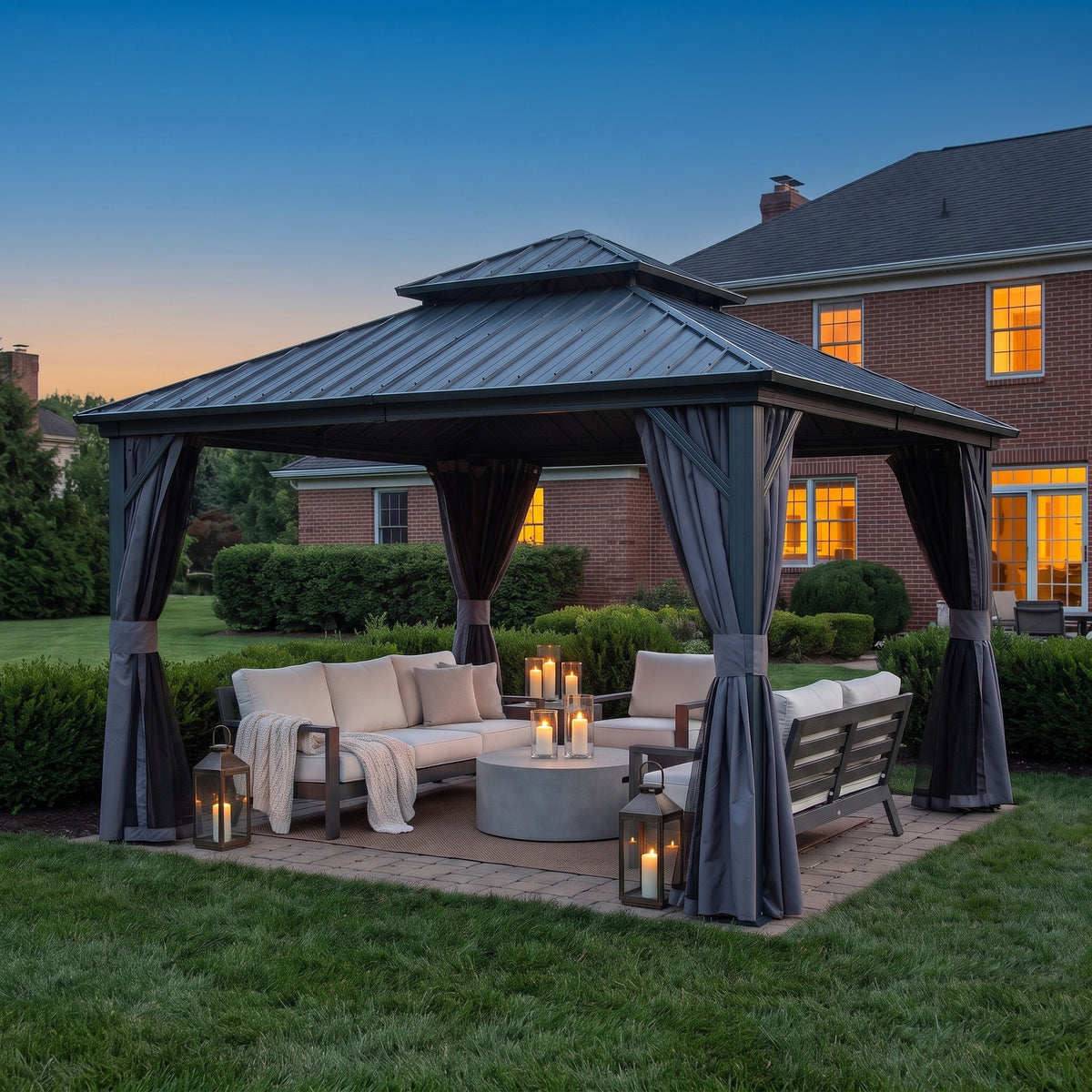 Gray aluminum 12x12 double roof gazebo with tied back curtains over a lounge set lit by lanterns at dusk