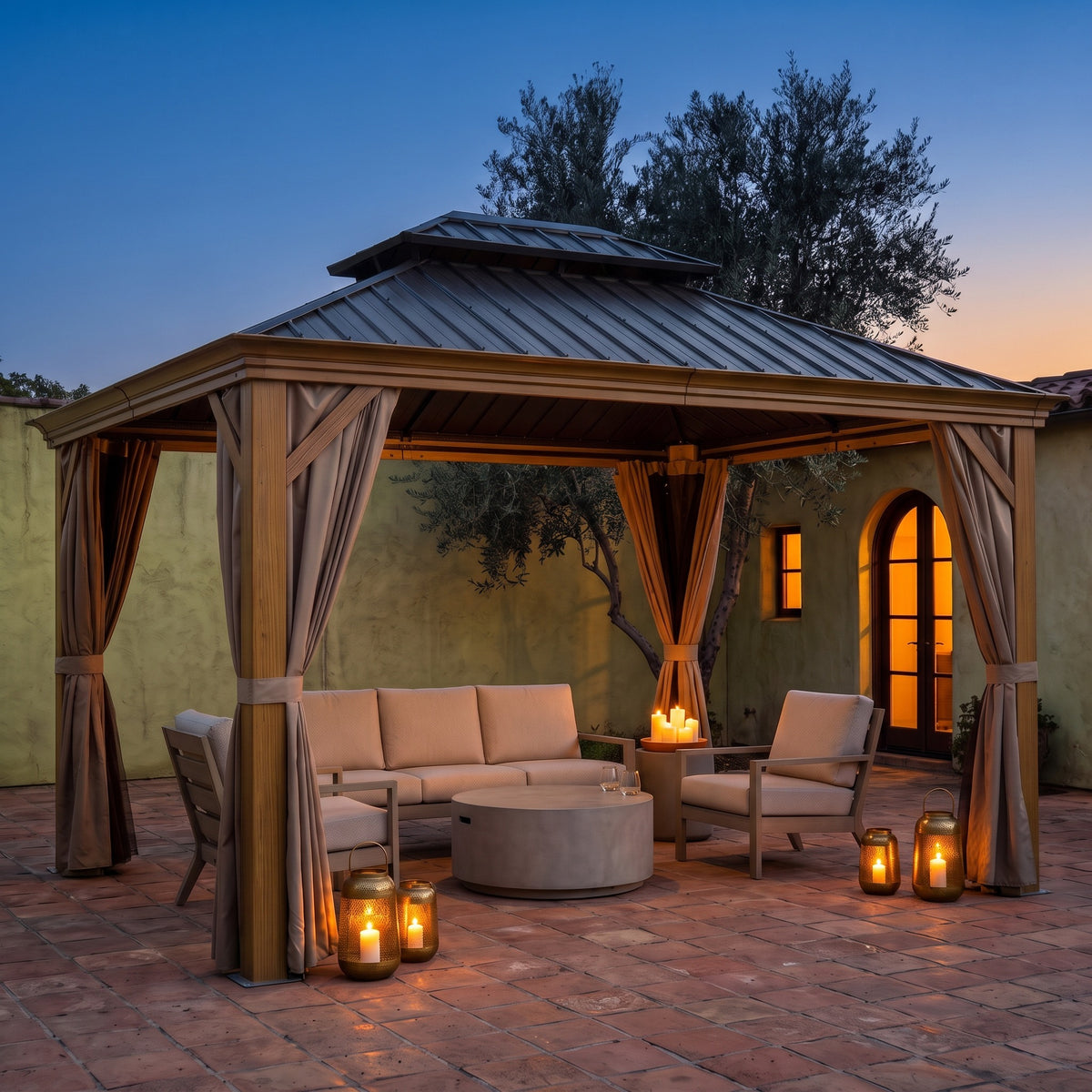 Wood-grain aluminum 12x14 hardtop gazebo with tan curtains over a sofa and lanterns on a tile courtyard at dusk