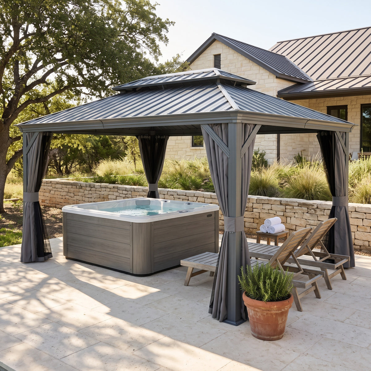 Gray hardtop gazebo with tied back curtains over a hot tub and wood loungers on a stone patio