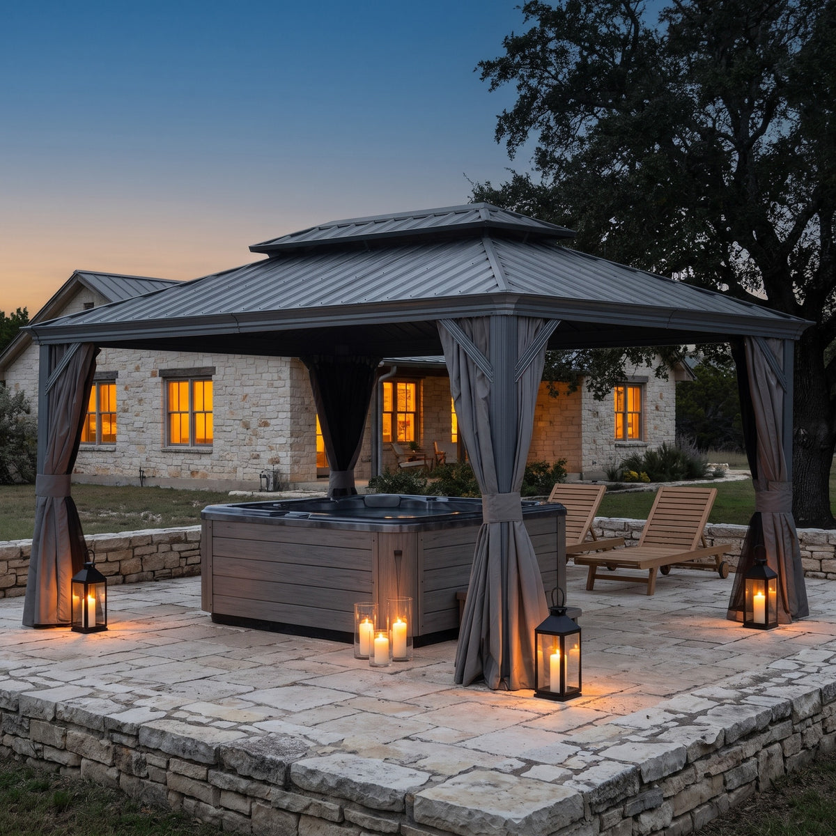Gray 12x16 hardtop gazebo with tied back curtains over a hot tub on a stone patio with candle lanterns at dusk