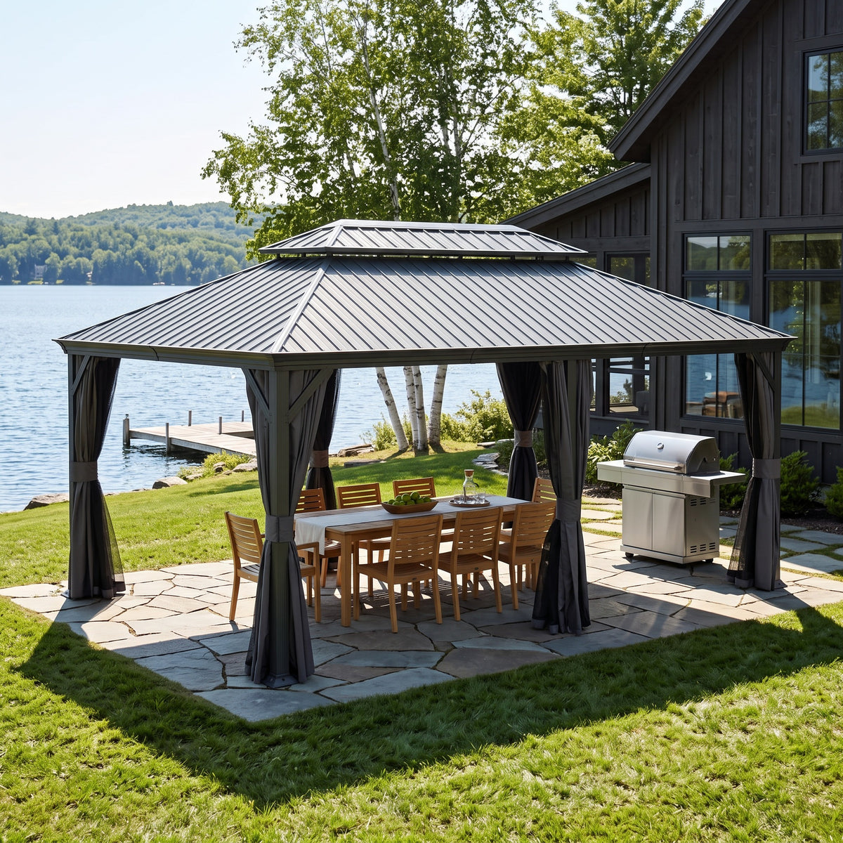 Dark gray 12x18 hardtop gazebo with tied back curtains over a teak dining table on a flagstone patio by a lake