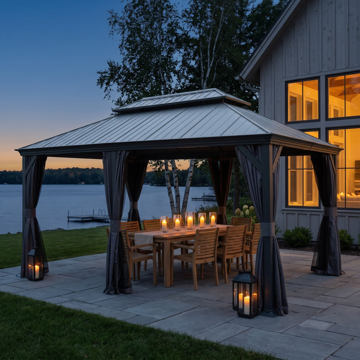Dark gray 12x18 hardtop gazebo with curtains tied back over a candlelit dining table on a lakeside patio at dusk