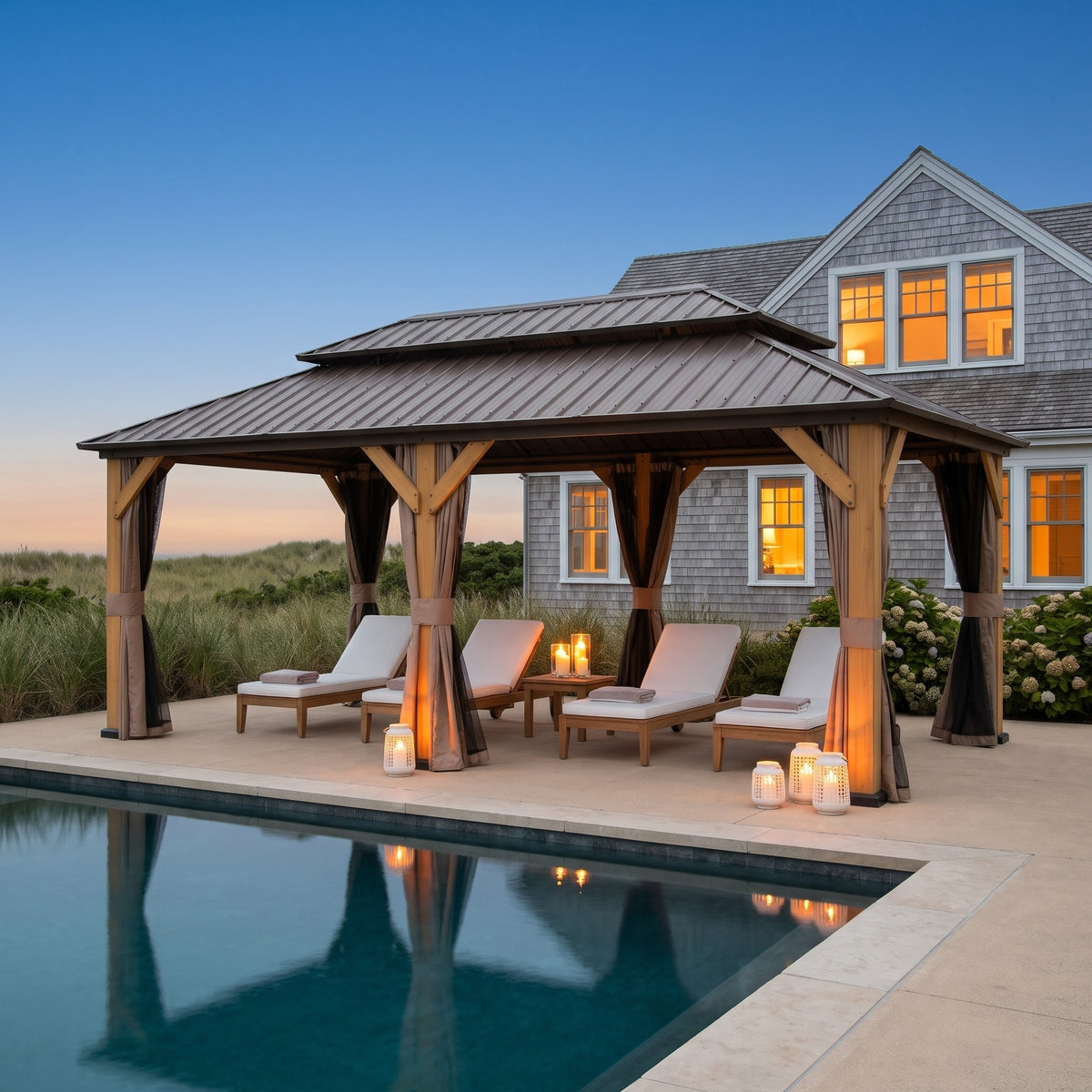 Brown cedar 12x20 hardtop gazebo with tied back curtains over pool loungers at dusk, lit by lanterns