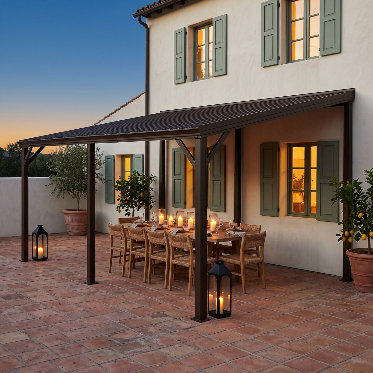 Brown metal 12x20 lean-to hardtop gazebo against a stucco house over a candlelit dining table at dusk