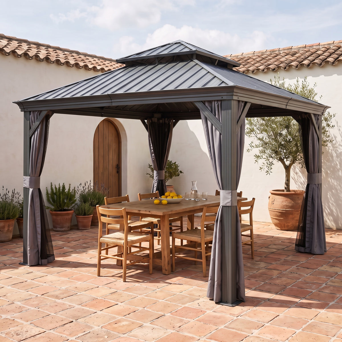 Gray steel 13x13 double roof hardtop gazebo with curtains over a wood dining table on a terracotta tile courtyard