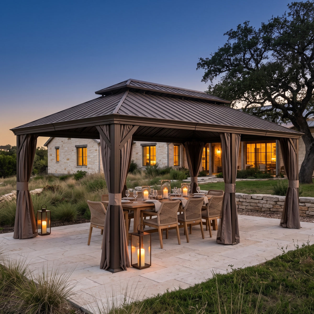Brown 14x20 hardtop gazebo with tied back curtains over a candlelit dining table on a stone patio at dusk