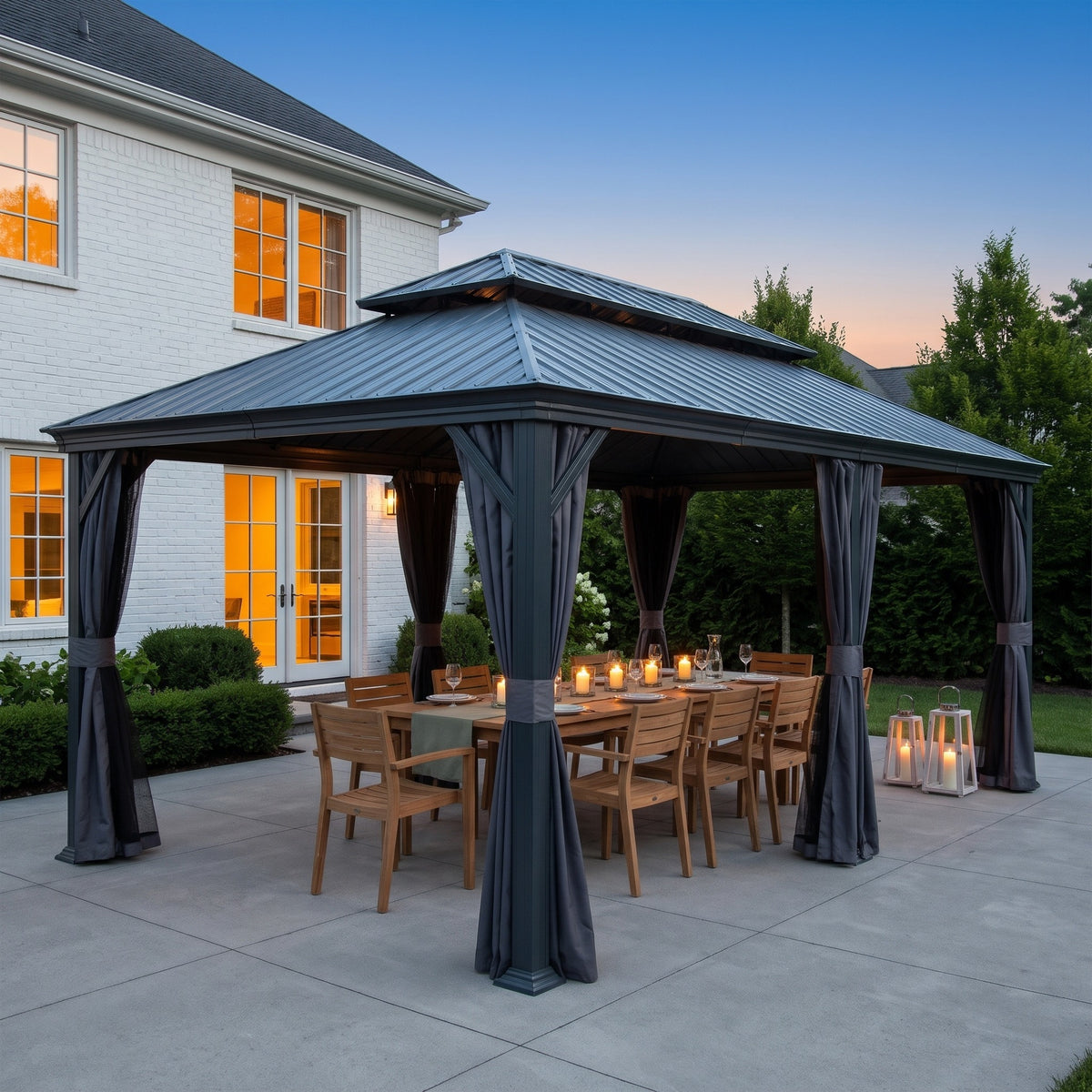 Dark gray metal hardtop gazebo with tied gray curtains over a teak dining table set with candles at dusk