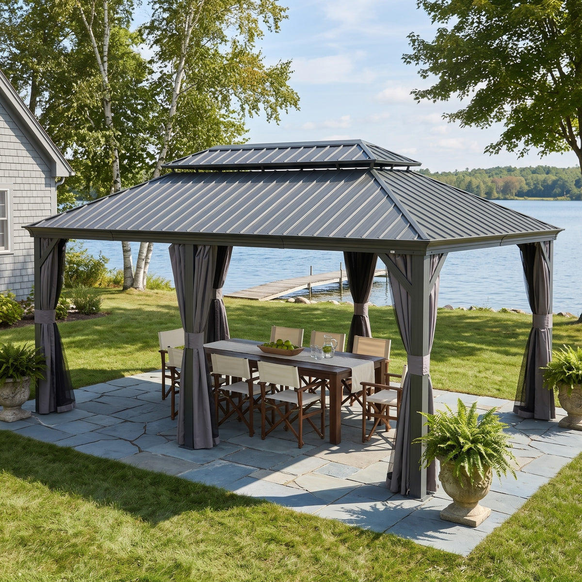 Gray aluminum 14x20 double roof hardtop gazebo with tied back curtains over a dining table on a lakeside stone patio