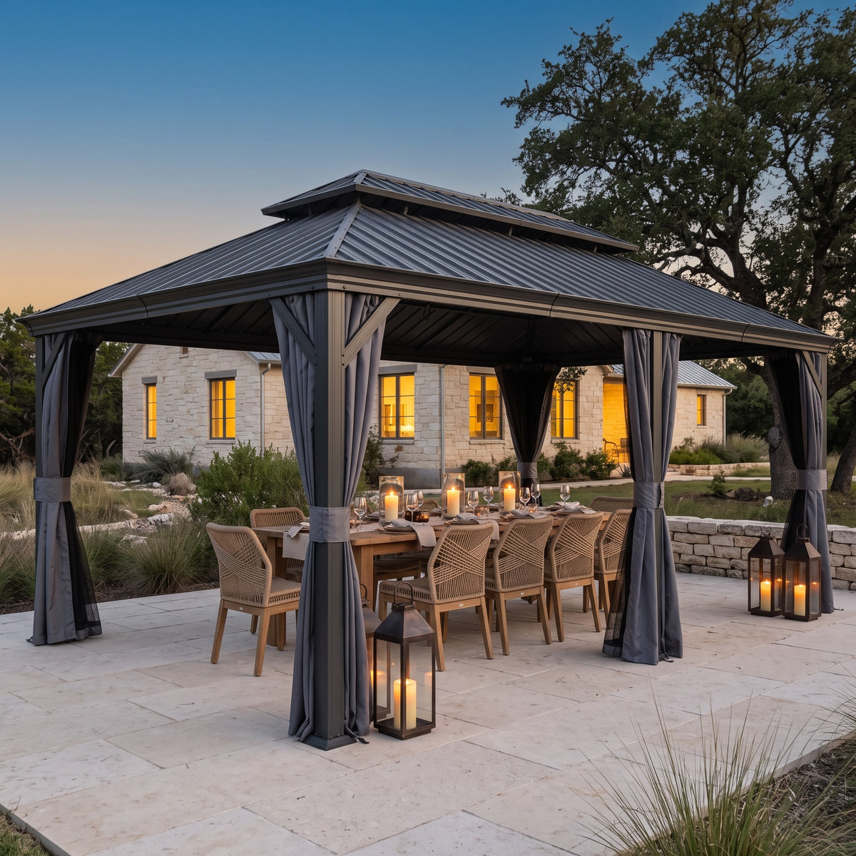 Gray aluminum 14x20 hardtop gazebo with tied back curtains over a dining table on a stone patio at dusk