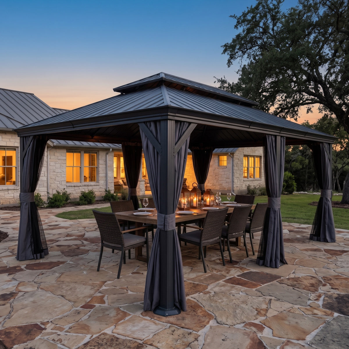 Dark gray double roof hardtop gazebo with curtains over a lantern lit dining table on a flagstone patio at dusk