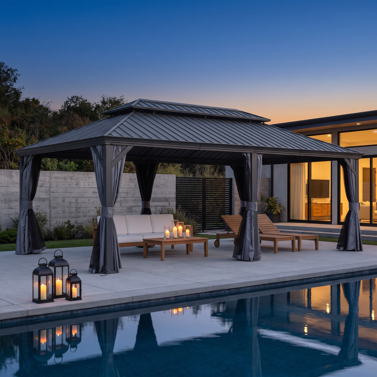 Gray 14x24 hardtop gazebo with tied back curtains over a sofa and loungers beside a pool at dusk