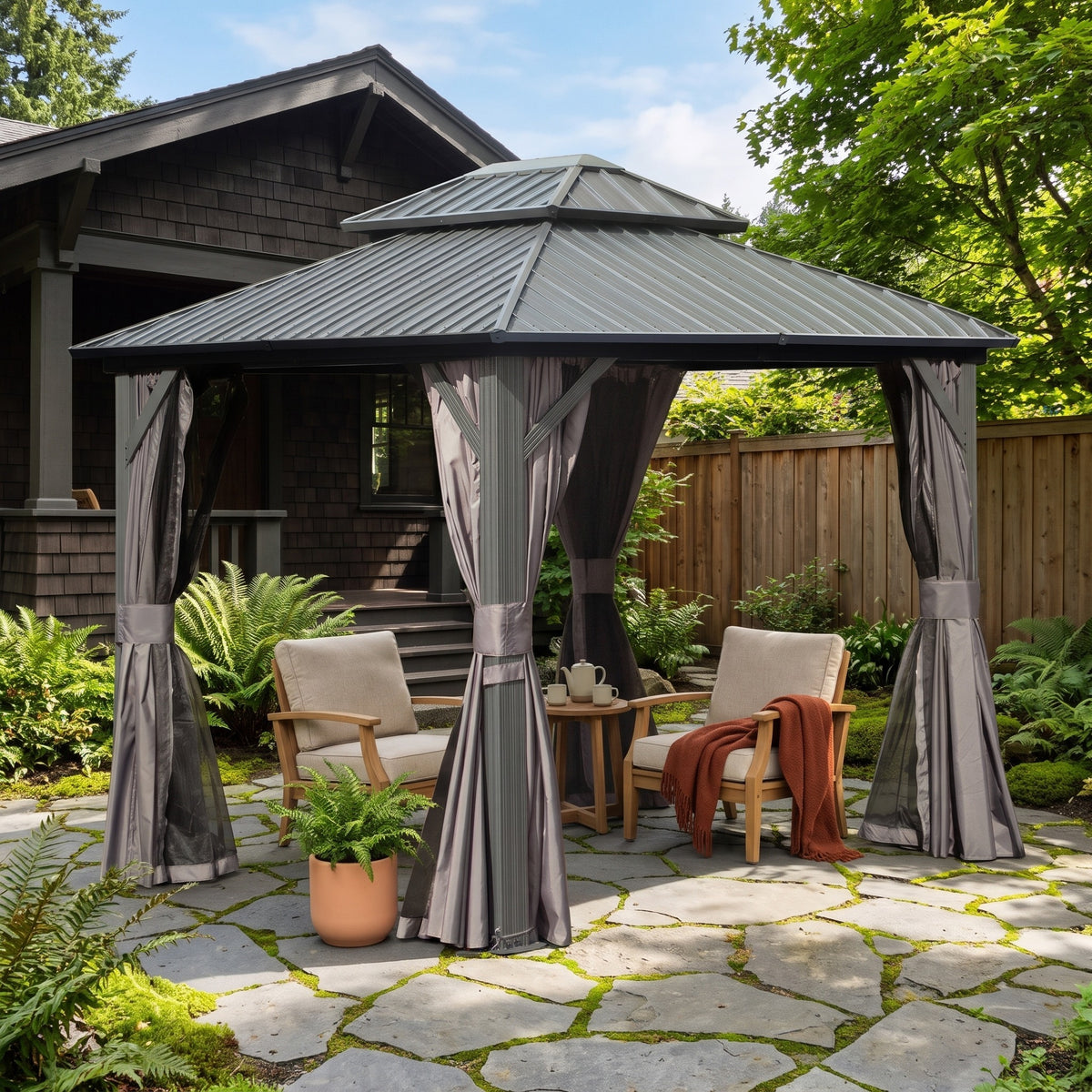 Gray double roof hardtop gazebo with tied back curtains over two wood lounge chairs on a flagstone patio