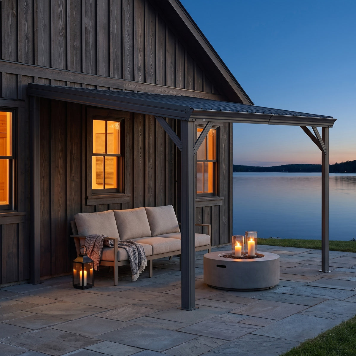 Gray metal 8x10 lean-to hardtop gazebo on a house wall over a sofa and candles on a stone patio at dusk