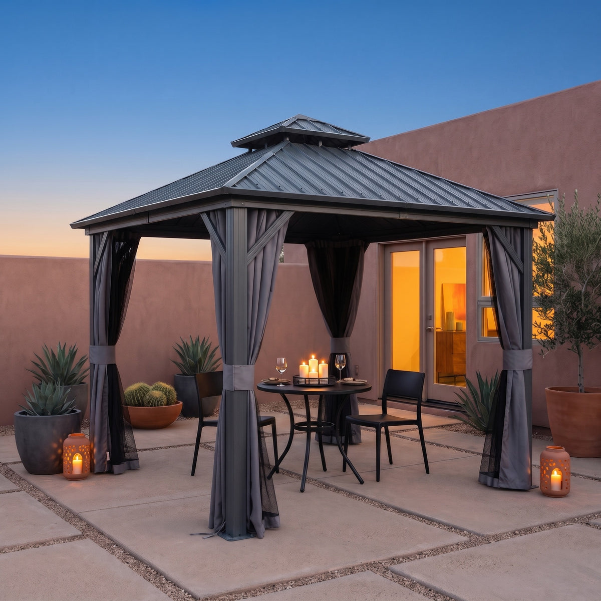 Gray aluminum 8x8 hardtop gazebo with tied back curtains over a candlelit bistro table on a desert patio at dusk