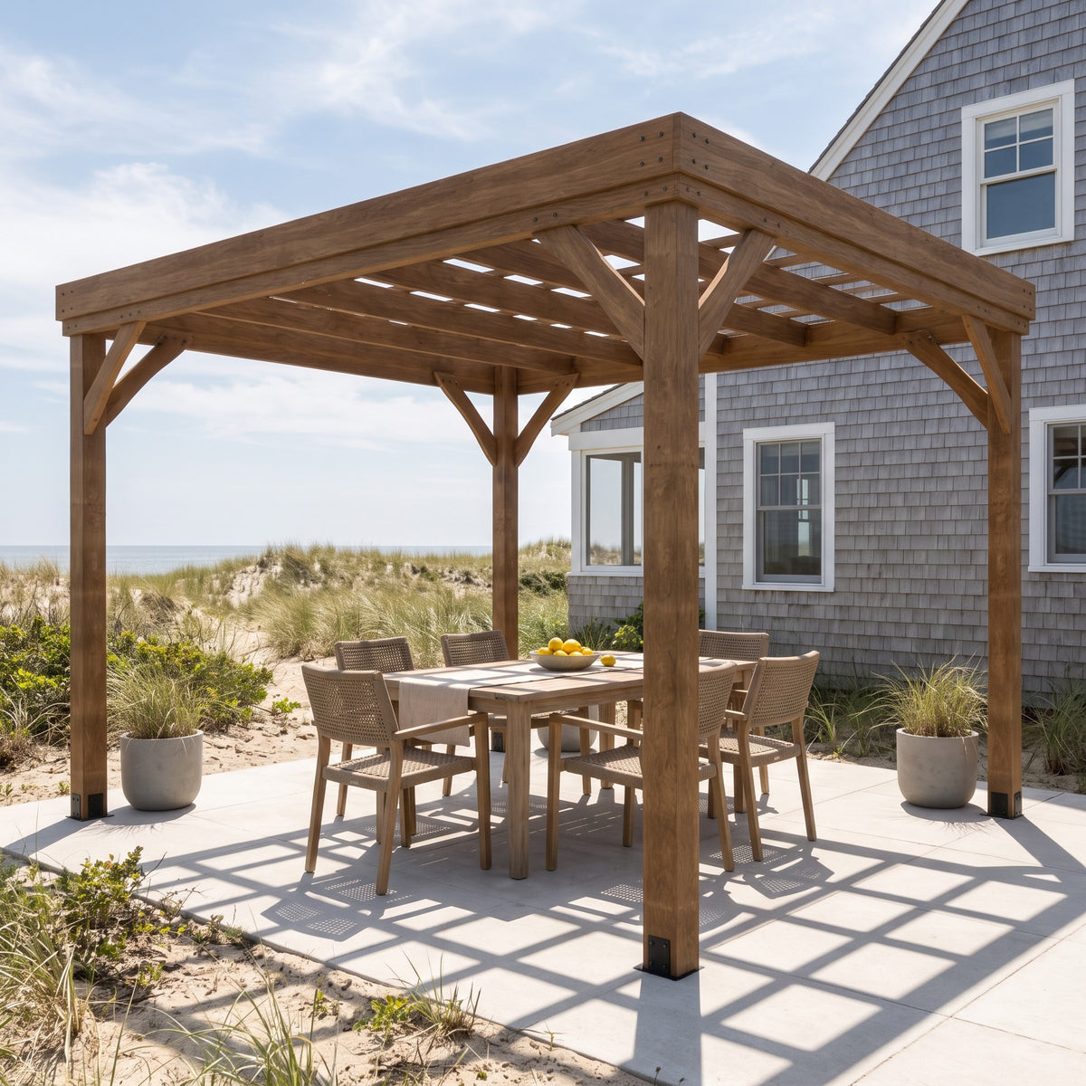 Brown wood pergola with open grid roof over a six seat dining table on a concrete patio by the dunes