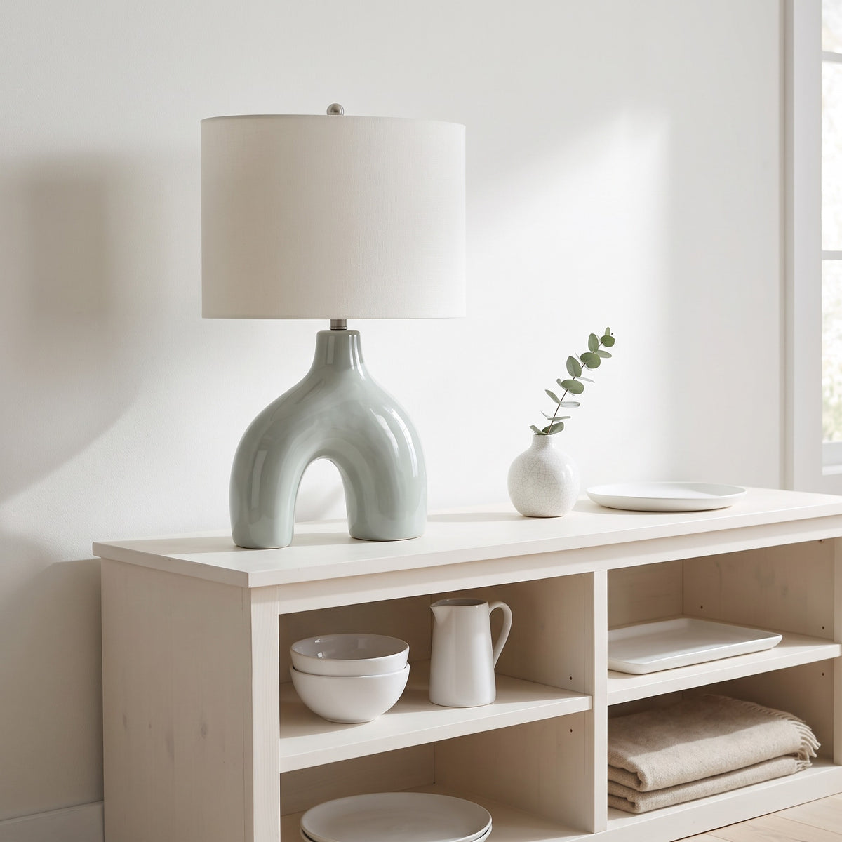 Green ceramic arch table lamp with ivory fabric shade on a white open shelf console