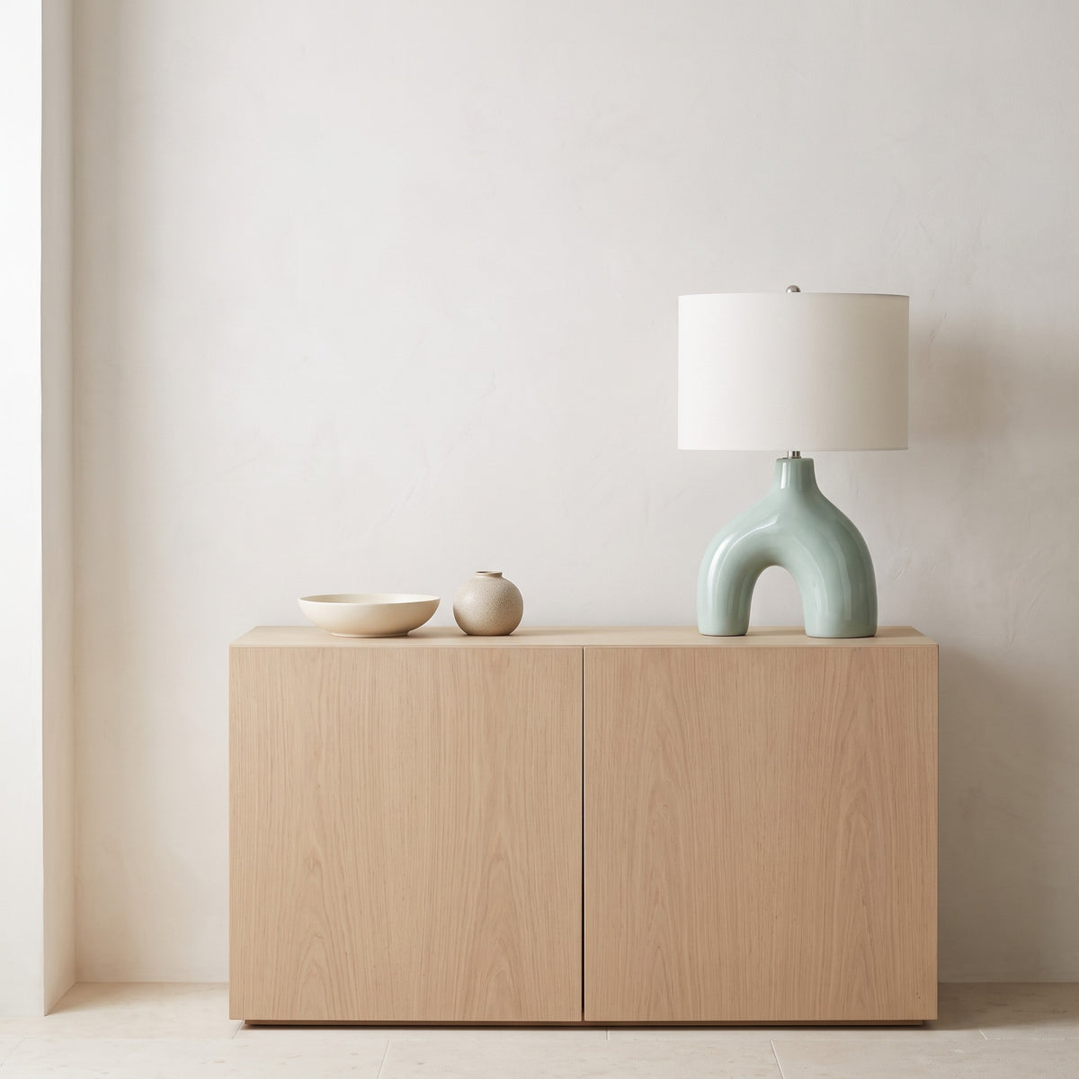 Light green ceramic arch table lamp with ivory fabric drum shade on a pale oak credenza