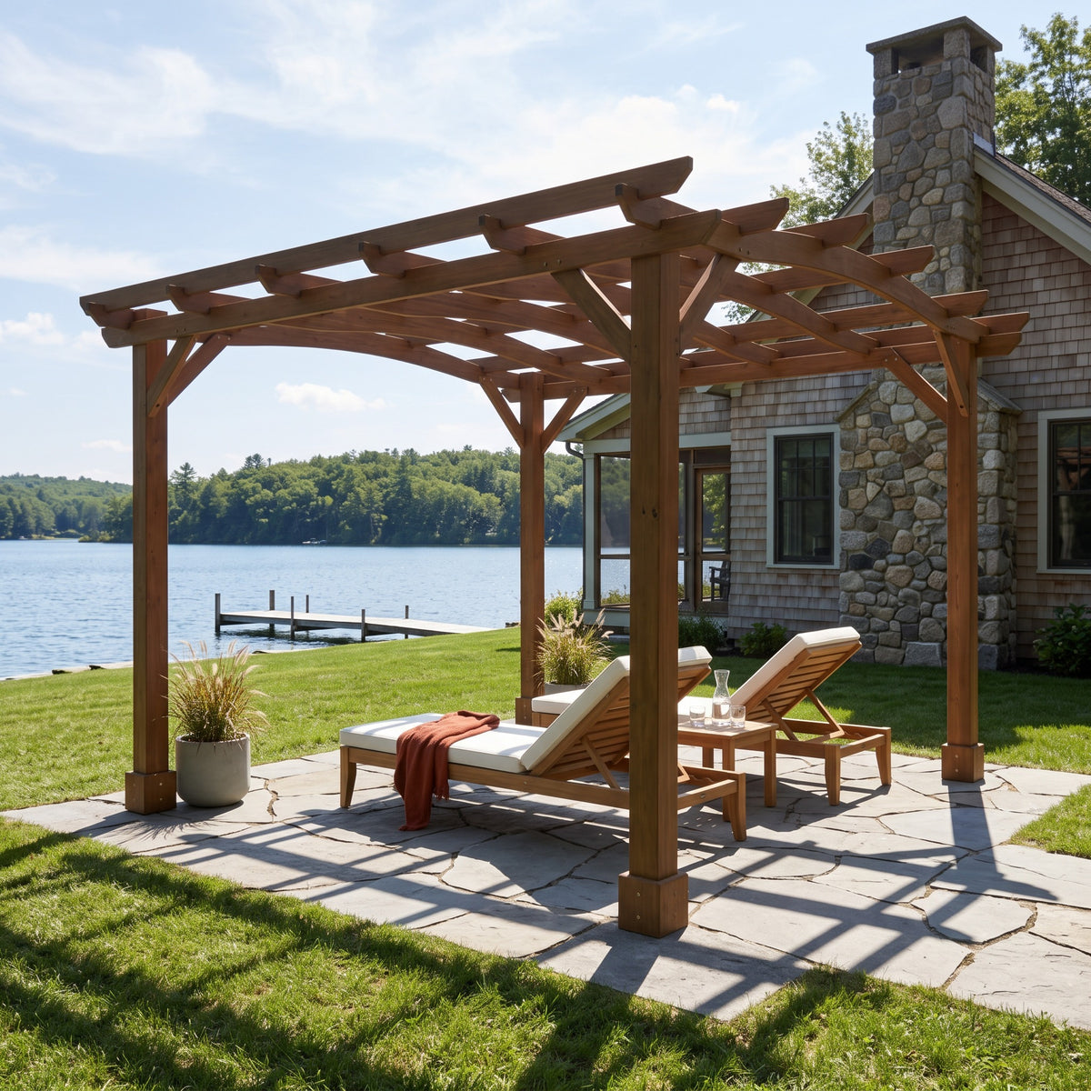 Dark brown fir pergola with a curved slatted roof over two lounge chairs on a stone patio by a lake