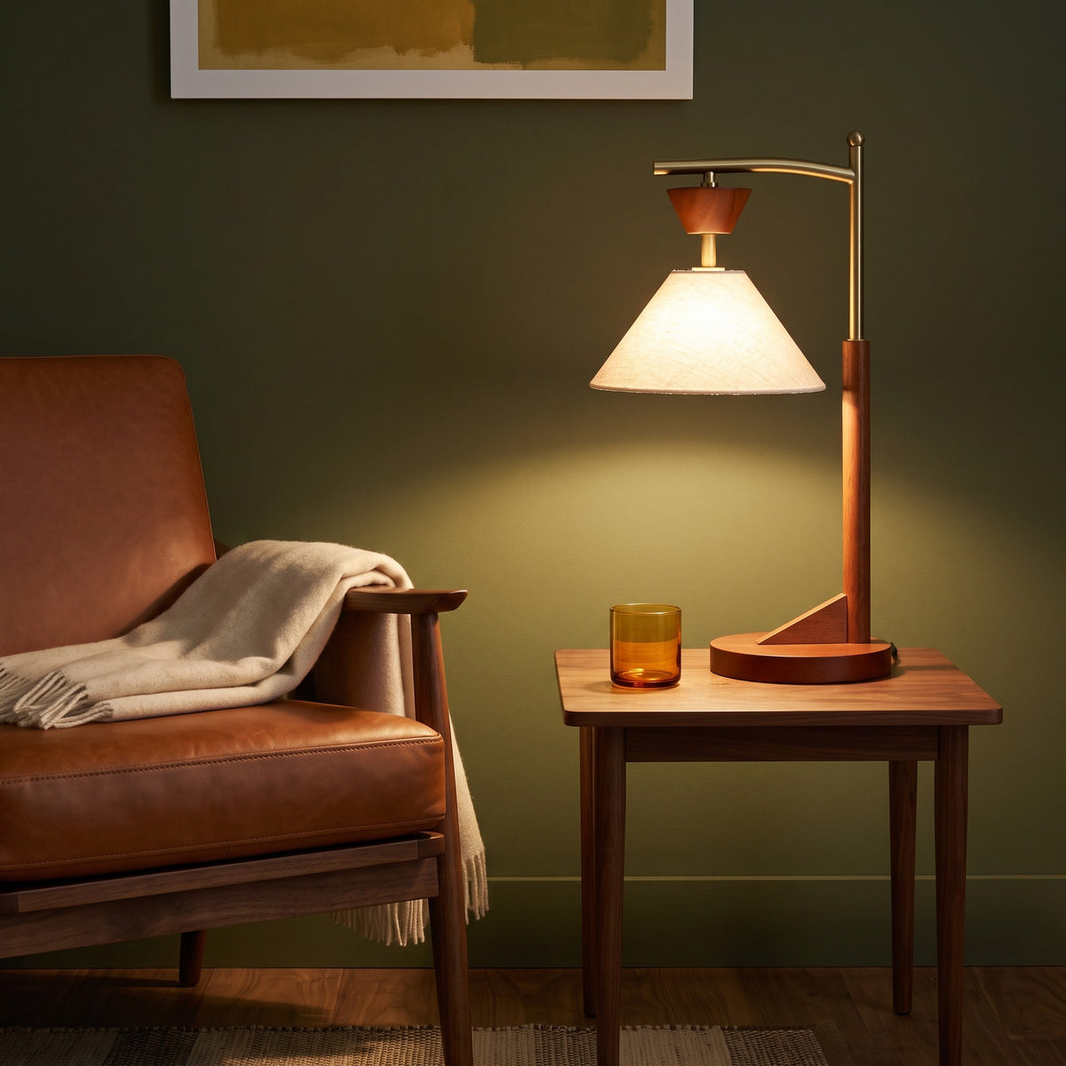 Brown wood and brass table lamp with lit linen-look cone shade on a walnut side table beside a leather lounge chair