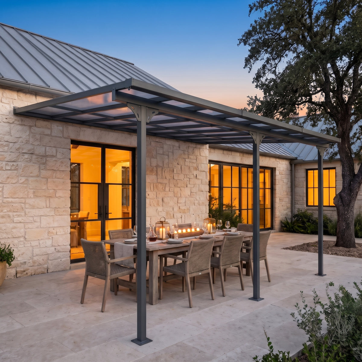 Gray aluminum wall mounted pergola with a polycarbonate roof over a candlelit dining table on a stone patio at dusk