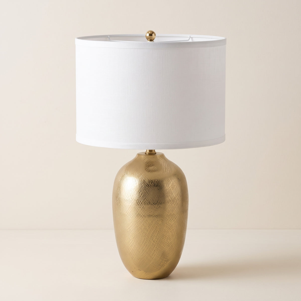 Gold etched urn table lamp with white linen-look drum shade on a warm ivory backdrop