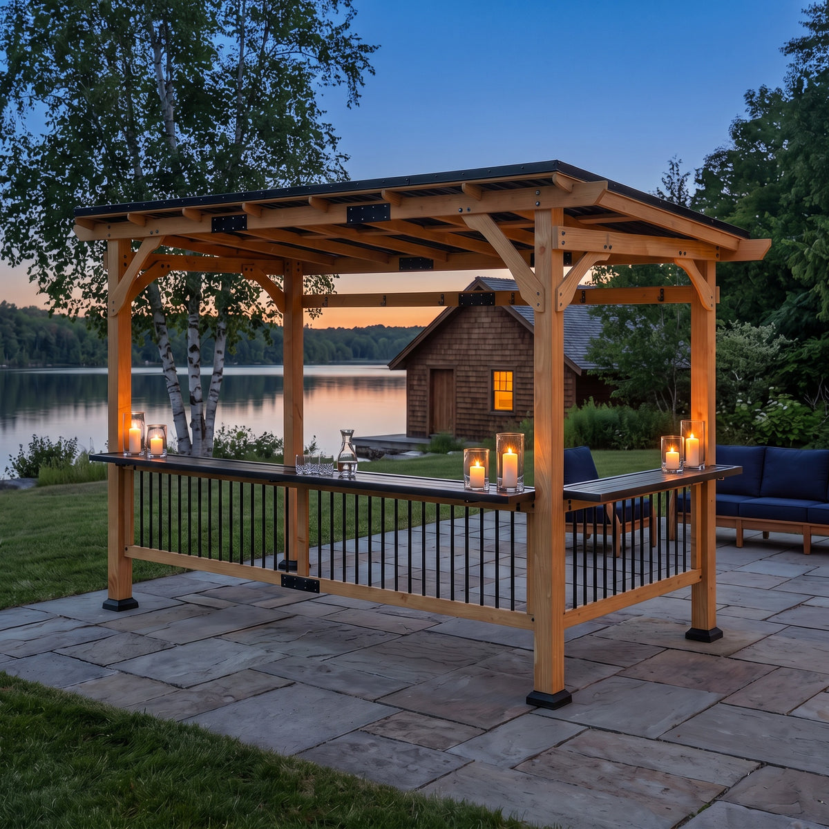 Natural wood gazebo with black metal pent roof and bar shelves lit by candles on a stone patio by a lake at dusk