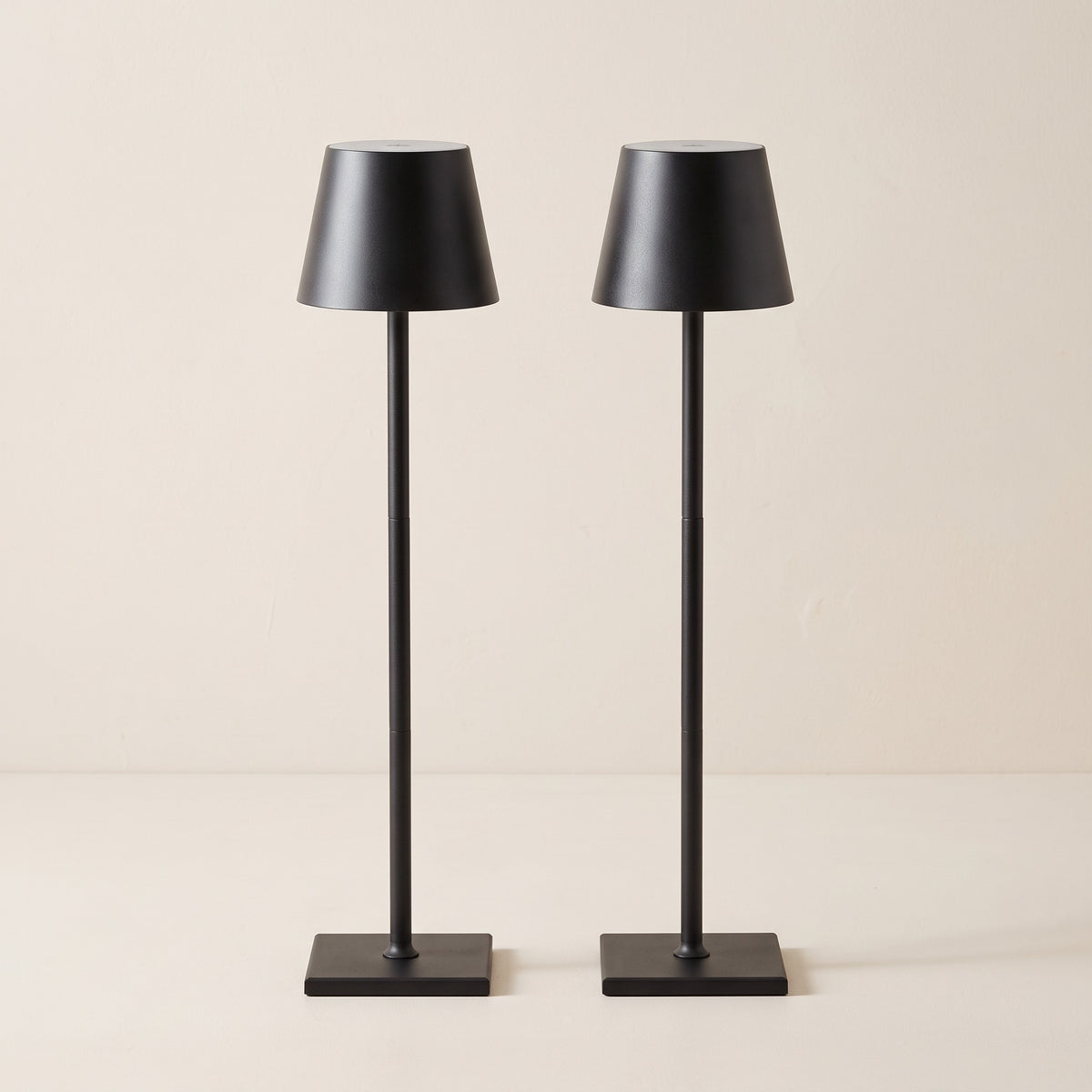 Set of two black cordless table lamps with tapered shades and square bases on an ivory backdrop