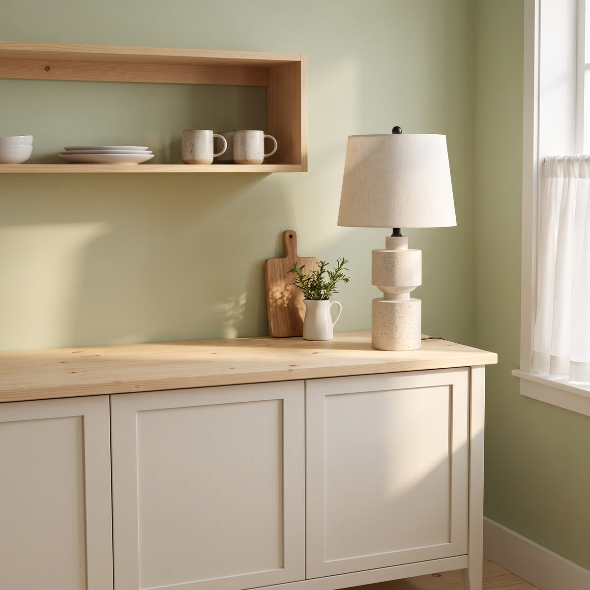 Beige speckled resin table lamp with linen-look tapered shade on a pine top sideboard in a sage green kitchen