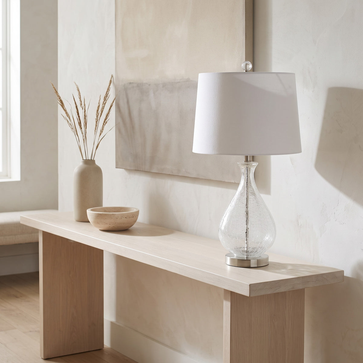 Clear crackle glass table lamp with white linen shade and nickel base on a light wood console