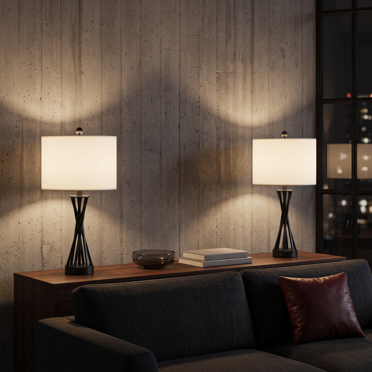 Pair of black metal table lamps with white linen shades lit on a walnut console behind a charcoal sofa