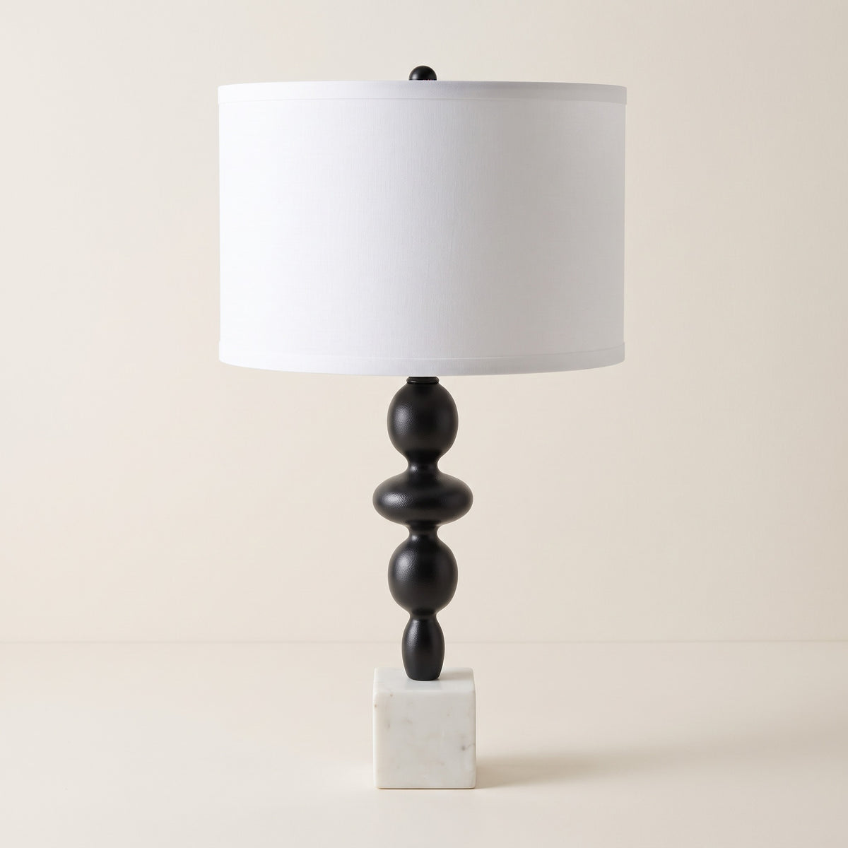 Black stacked table lamp with white marble cube base and white linen-look drum shade on an ivory backdrop