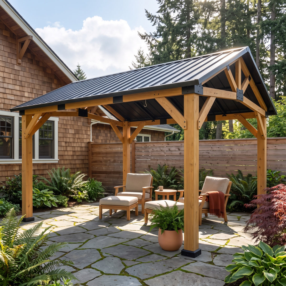 Wood hardtop gazebo with black metal gable roof over lounge chairs on a flagstone patio beside a shingled house