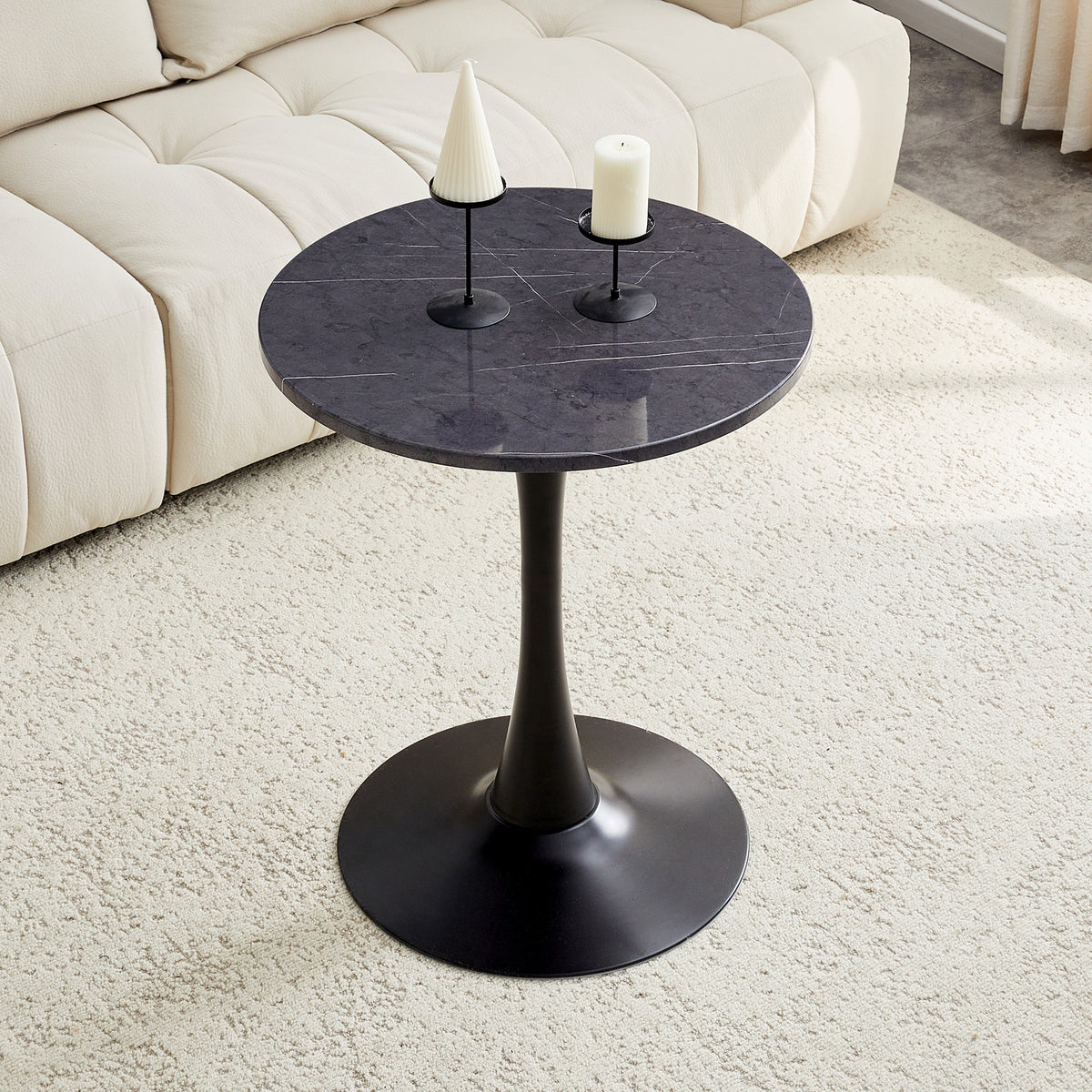 Black marble-look bistro table with two candle holders beside a cream tufted sofa, high angle view