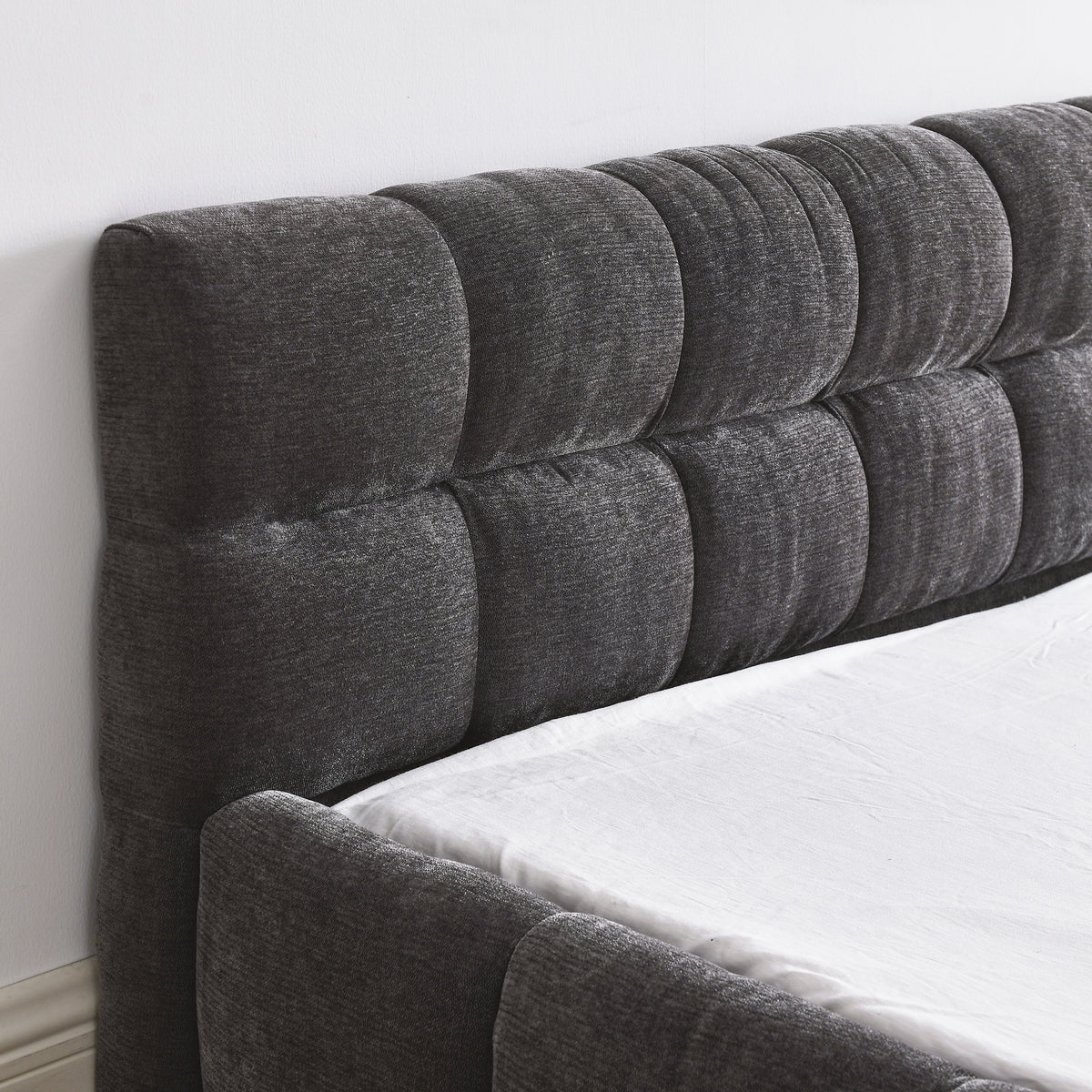 Close-up of the dark grey chenille channel-tufted headboard corner