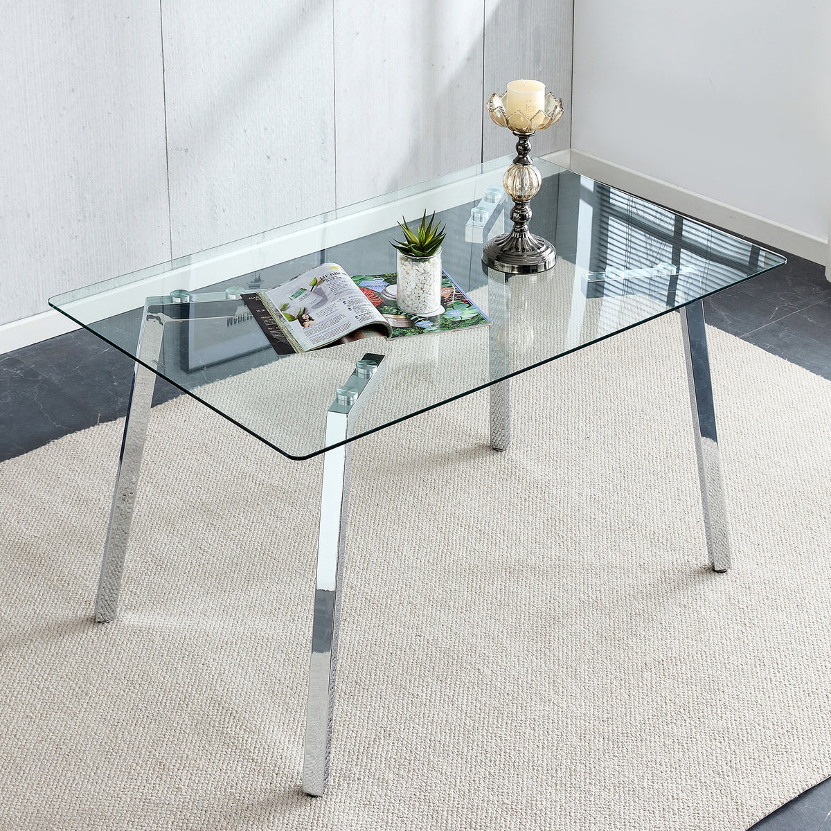 Rectangular glass dining table with angled chrome legs styled overhead with a magazine, plant and candle holder
