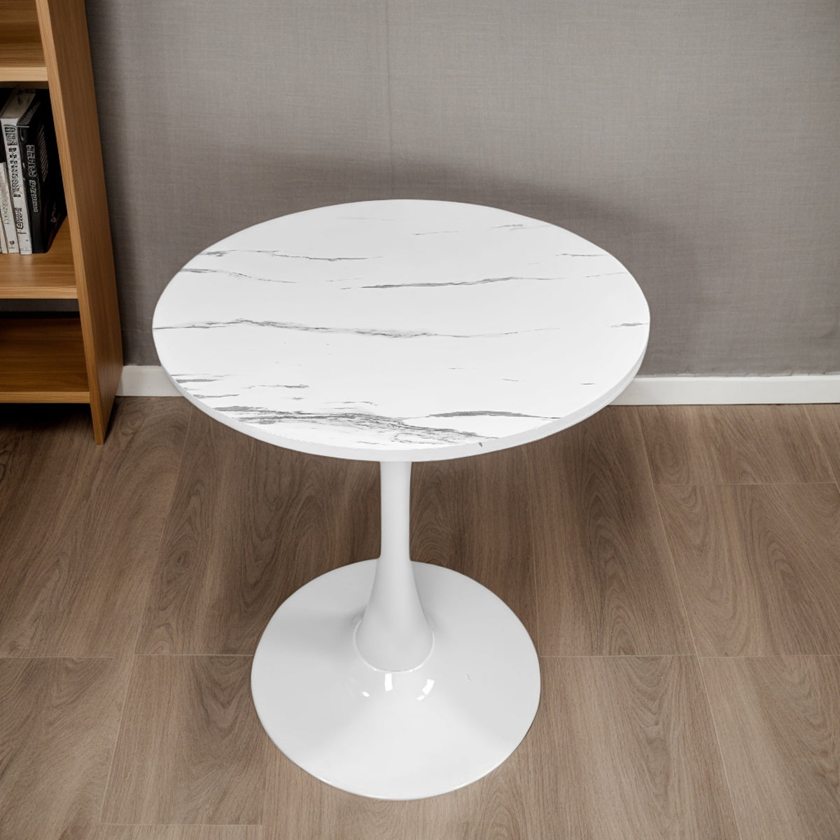 White marble tulip bistro table on wood flooring beside a bookshelf, three-quarter view