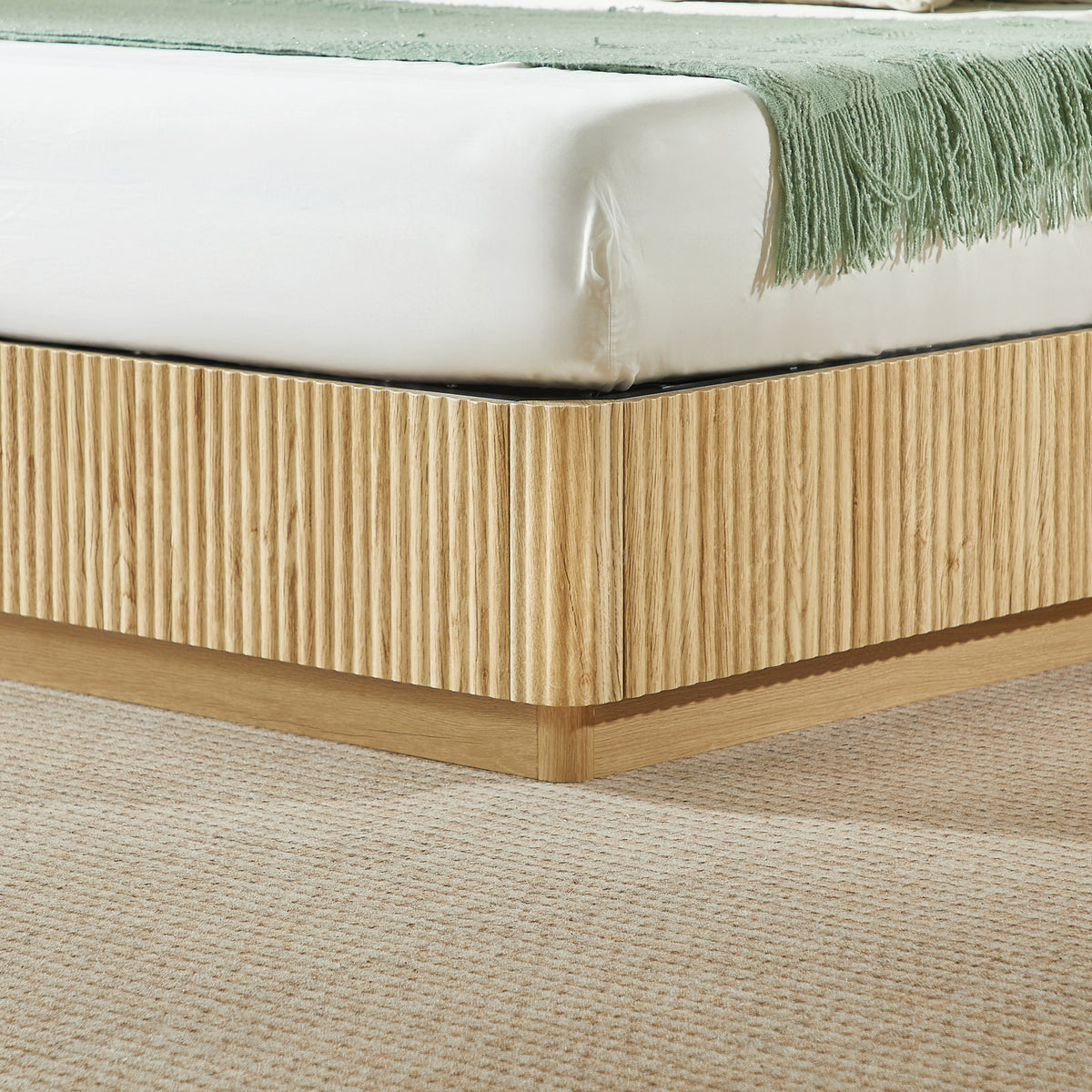 Closeup of the light oak fluted base corner and mattress edge with green fringed throw